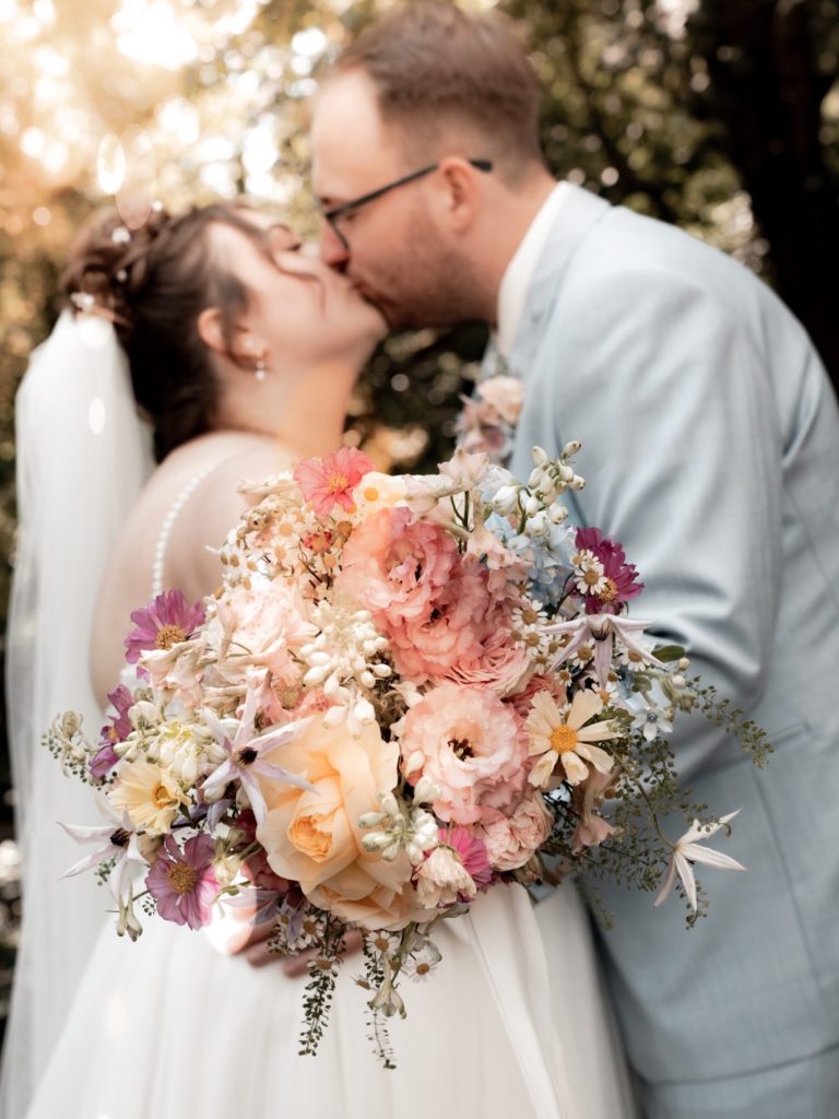 Paar in eleganter Hochzeitskleidung, umarmend am Wasser mit einer romantischen Atmosphäre.