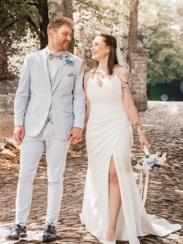 Paar in eleganter Hochzeitskleidung, umarmend am Wasser mit einer romantischen Atmosphäre.